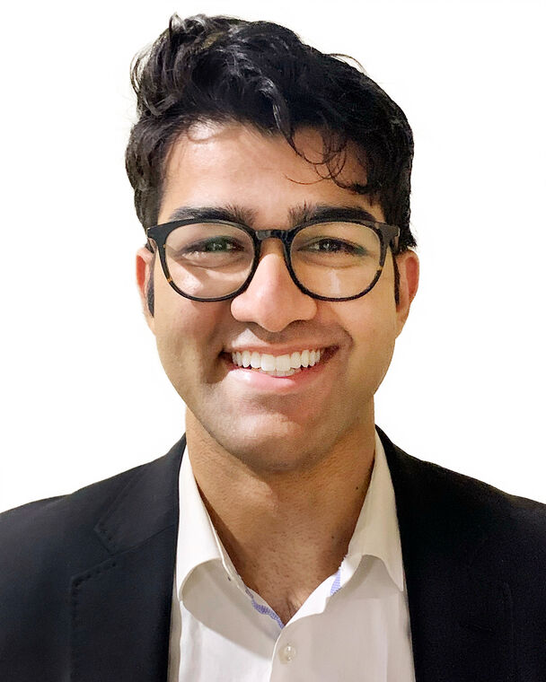 A headshot of Nathan Mallipeddi who is smiling at the camera and wearing a white collared shirt and black blazer.