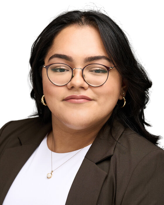 A headshot of Cinthia Zavala Ramos who is looking at the camera and wearing glasses, a white shirt, and a brown blazer.
