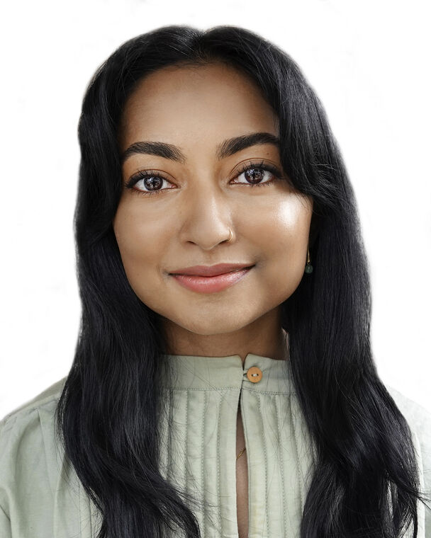 A headshot of Shyamala Ramakrishna who is staring at the camera with a closed-lp smile and wearing a light green-grey shirt with a buttoned collar.