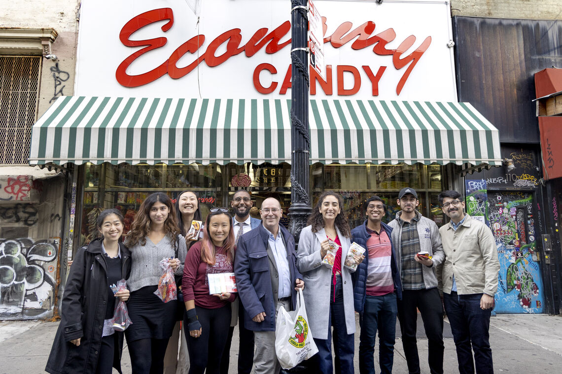 A group photo of nine Paul & Daisy Soros Fellows standing outside of Economy Candy with Director Craig Harwood.
