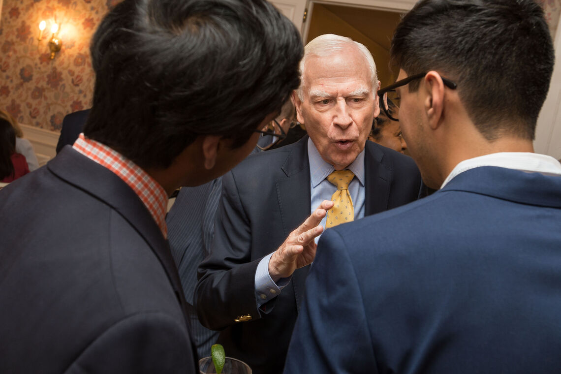 Board member Peter Georgescu talking with two 2022 Paul & Daisy Soros Fellows, all are in suits and the photo is taken from behind the two Fellows.